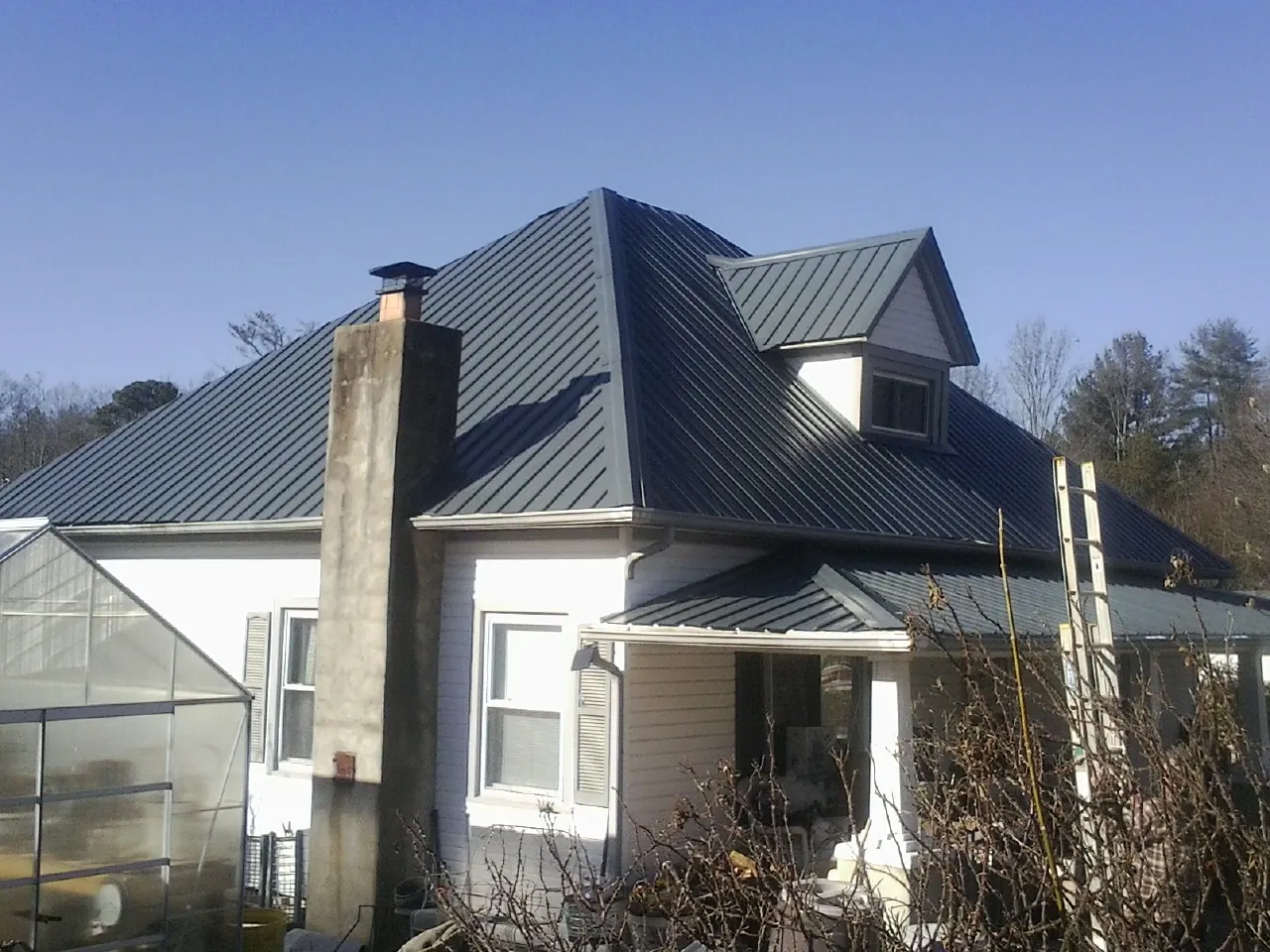 Dark blue standing seam metal roof on a white farmhouse with dormer — Slate & Tile Roof Repair by Roofing Brothers in Saint Clairsville