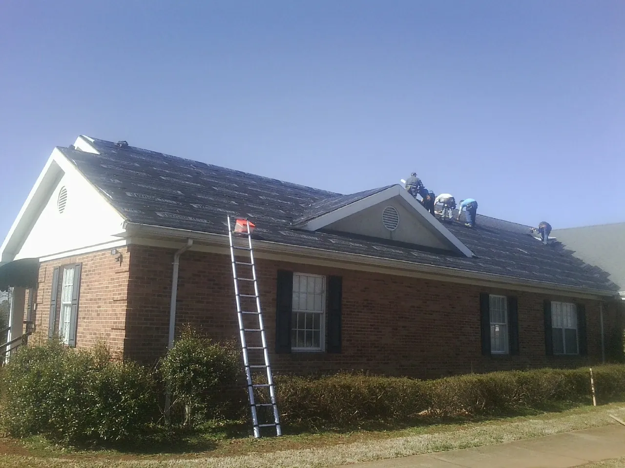 Crew tearing shingles off a brick ranch roof with a ladder set — Metal Roof Repair work by our crew in Saint Clairsville