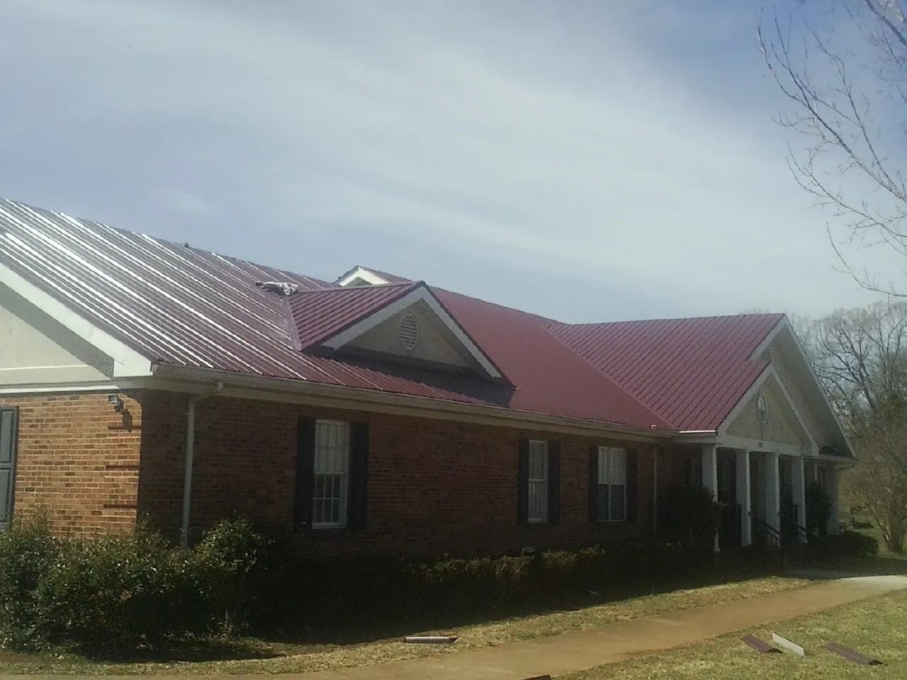 Red metal roof with gabled entries on a long brick building, from a Hail Damage Roof Repair job in Saint Clairsville
