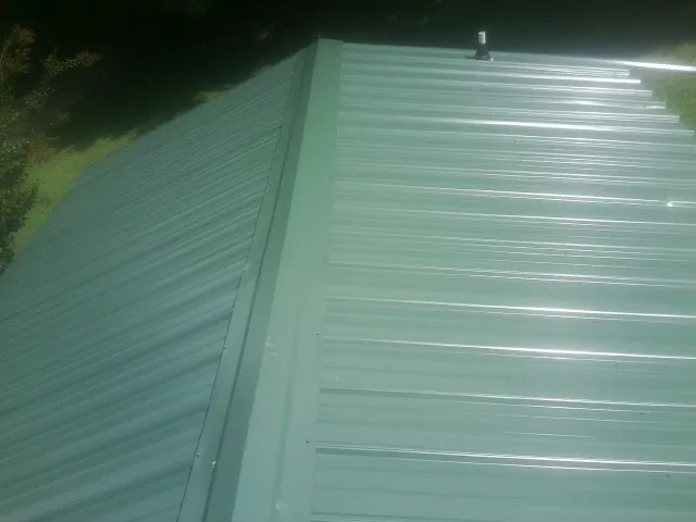 New green metal panels meeting at the ridge of a roof — Flat Roof Repair work by our crew in Saint Clairsville