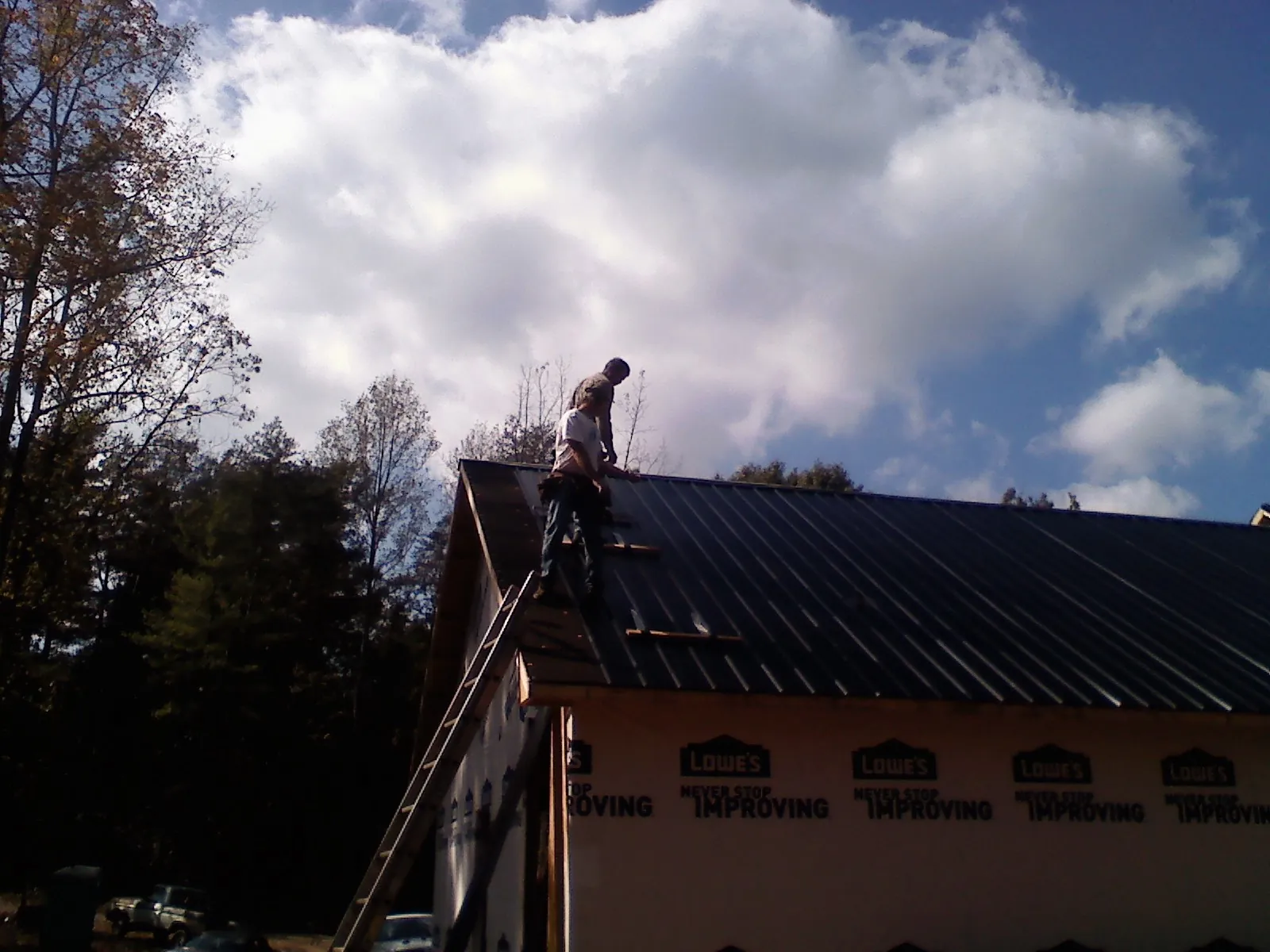 Roofer fastening dark metal panels high against a cloudy sky, from a Roof Inspection job in Saint Clairsville