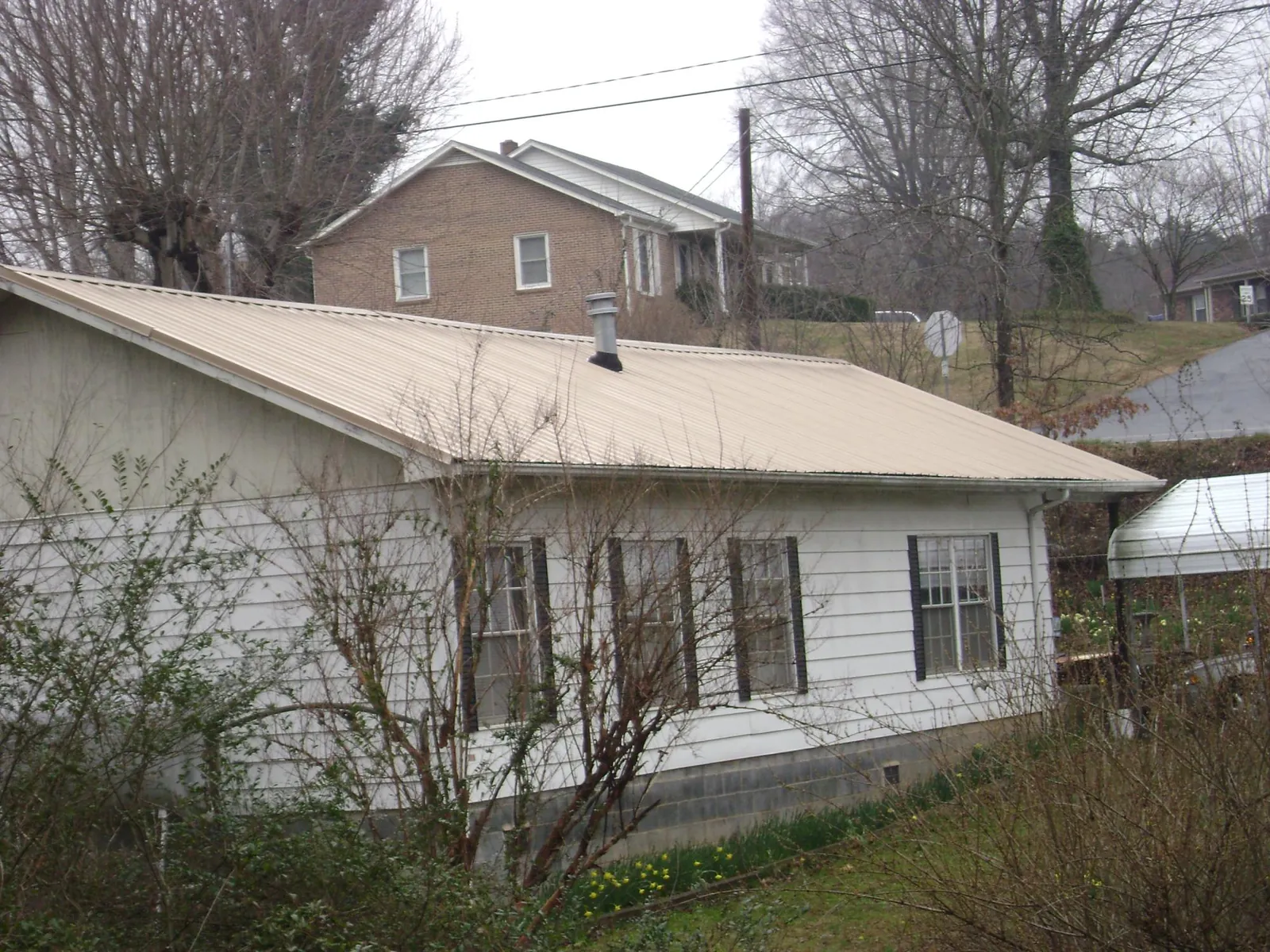 Tan metal roof on a white sided house set into a hillside — Commercial Roofing by Roofing Brothers in Saint Clairsville