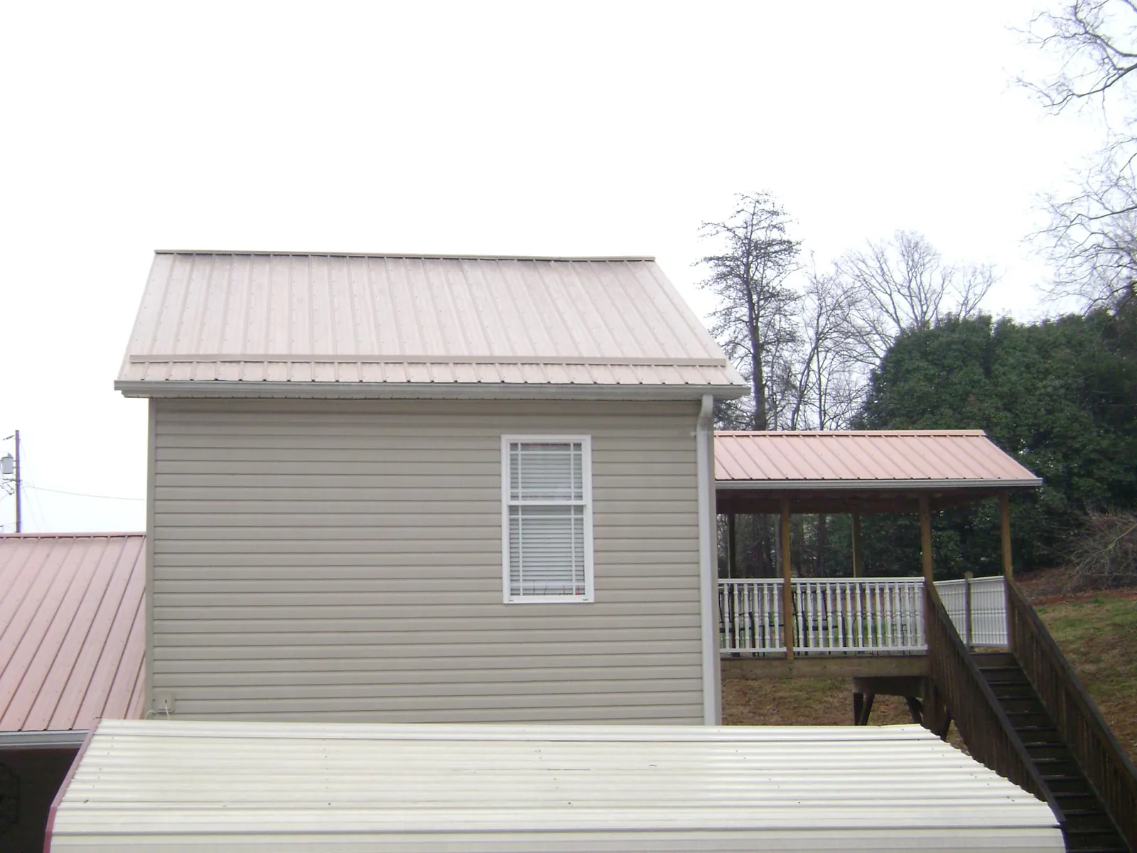 Tan metal roofs on a two story addition and attached porch, from a Roof Replacement job in Saint Clairsville